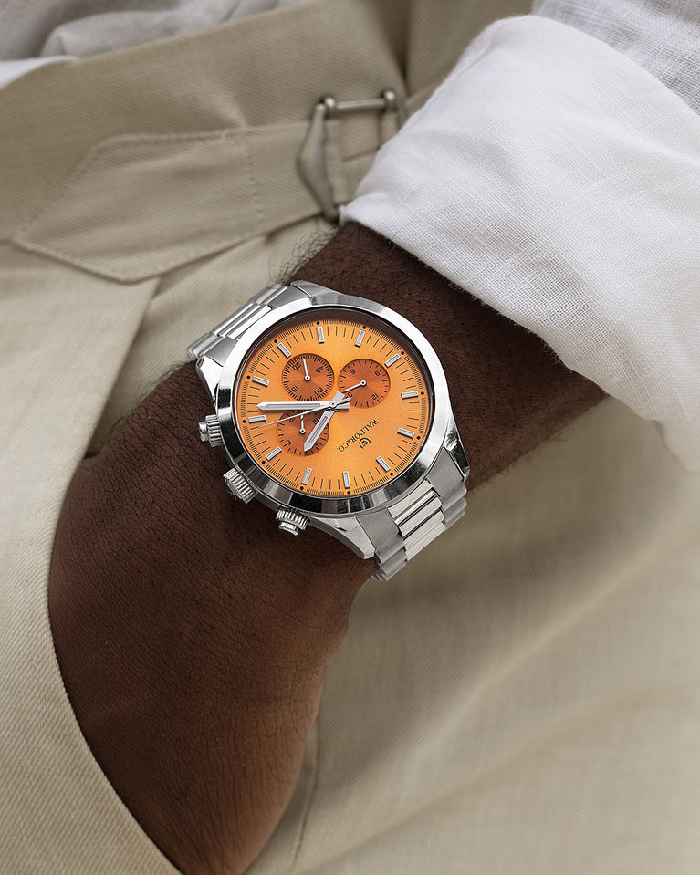 A round mens watch in rhodium-plated silver from Waldor & Co. with orange sunray dial and a second hand. Seiko movement. The model is Chrono 44 Como 44mm.