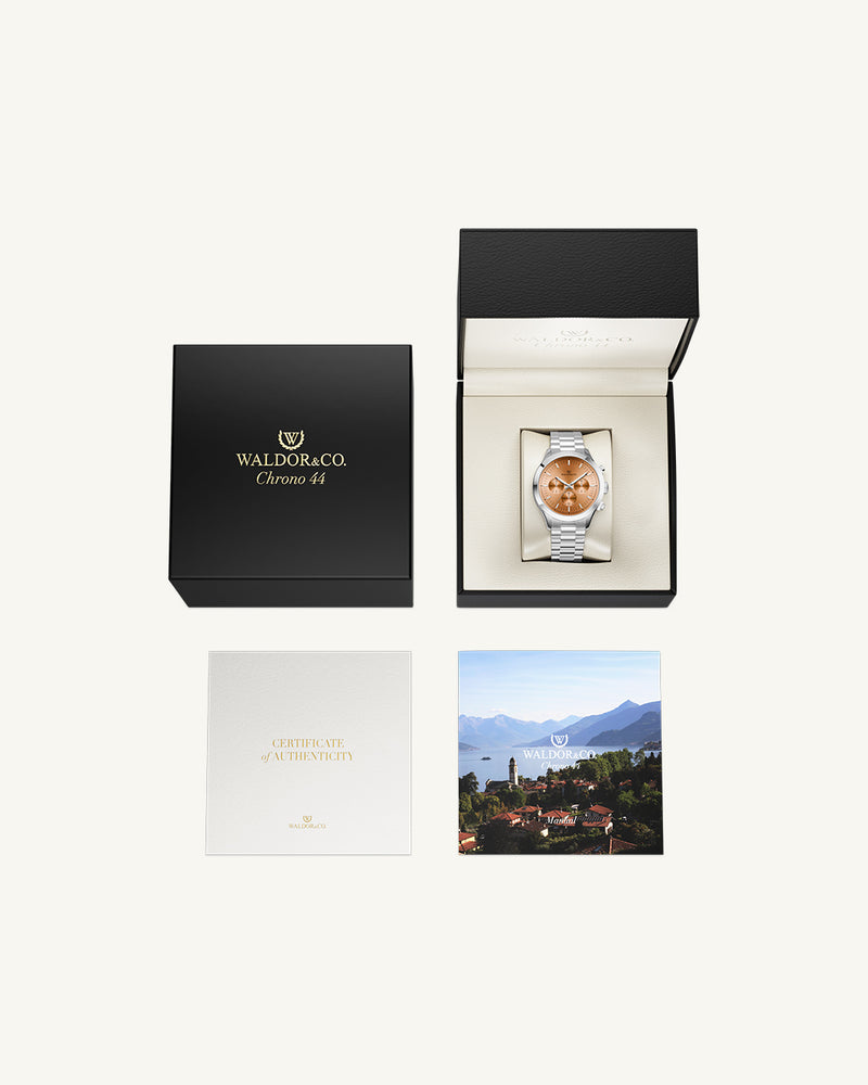 A round mens watch in rhodium-plated silver from Waldor & Co. with orange sunray dial and a second hand. Seiko movement. The model is Chrono 44 Como 44mm.