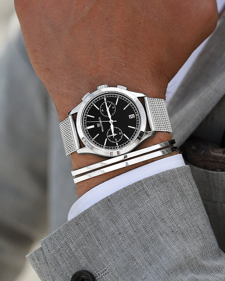 En rund herrklocka i rodiumpläterat silver från WALDOR & CO. med svart sunray urtavla och en sekundvisare. Seiko urverk. Modellen är Chrono 44 Sardinia 44mm.