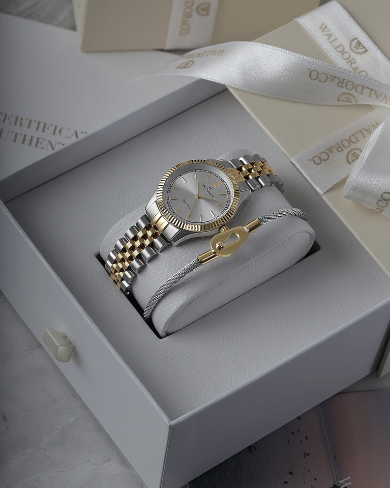 A round womens watch in silver and 22k gold from Waldor & Co. with silver sunray dial and a second hand. Seiko movement. The model is Imperial 32 Positano 32mm.