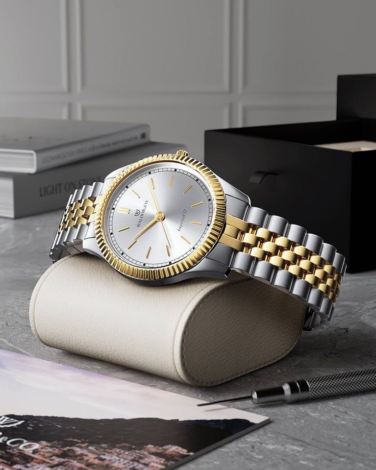 A round womens watch in silver and 22k gold from Waldor & Co. with silver sunray dial and a second hand. Seiko movement. The model is Imperial 32 Positano 32mm.