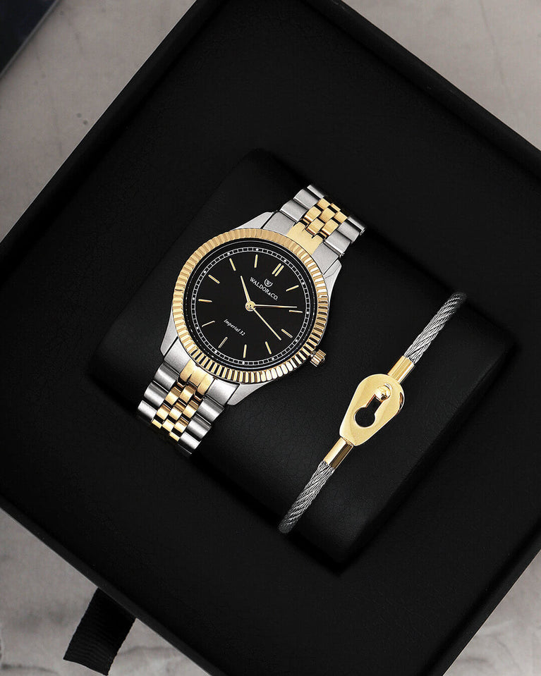 A round womens watch in silver and 14k gold from Waldor & Co. with black sunray dial and a second hand. Seiko movement. The model is Imperial 32 Positano 32mm.